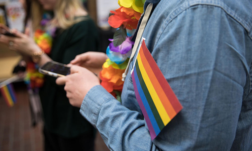 student texting while holding a small pride flag in the crook of their arm