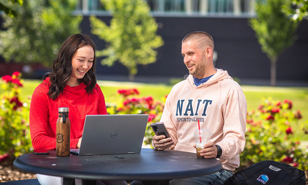 female and male student sitting in quad at a table with a laptop