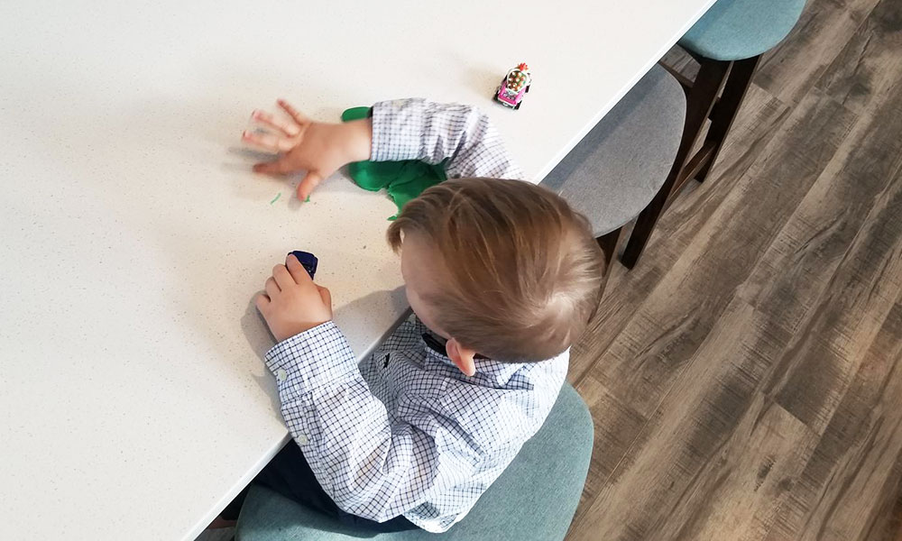 little boy sitting at table playing with toy cars and playdough