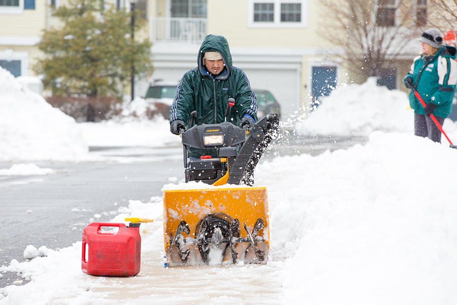 man using gas-powered snow blower to clear sidewalk