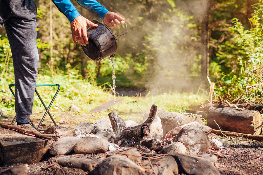 man putting out campfire with pot full of water