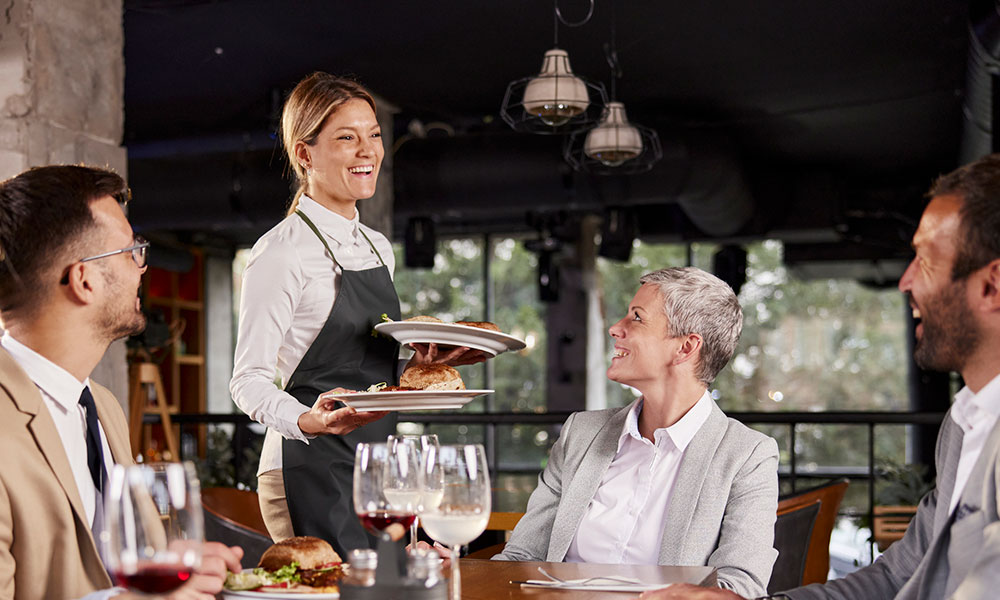 server smiling while bringing food to table of people at a restaurant