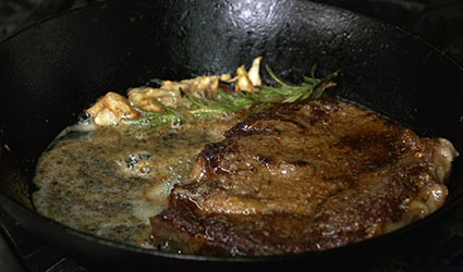 A steak perfectly grilled on a stovetop with rosemary and butter
